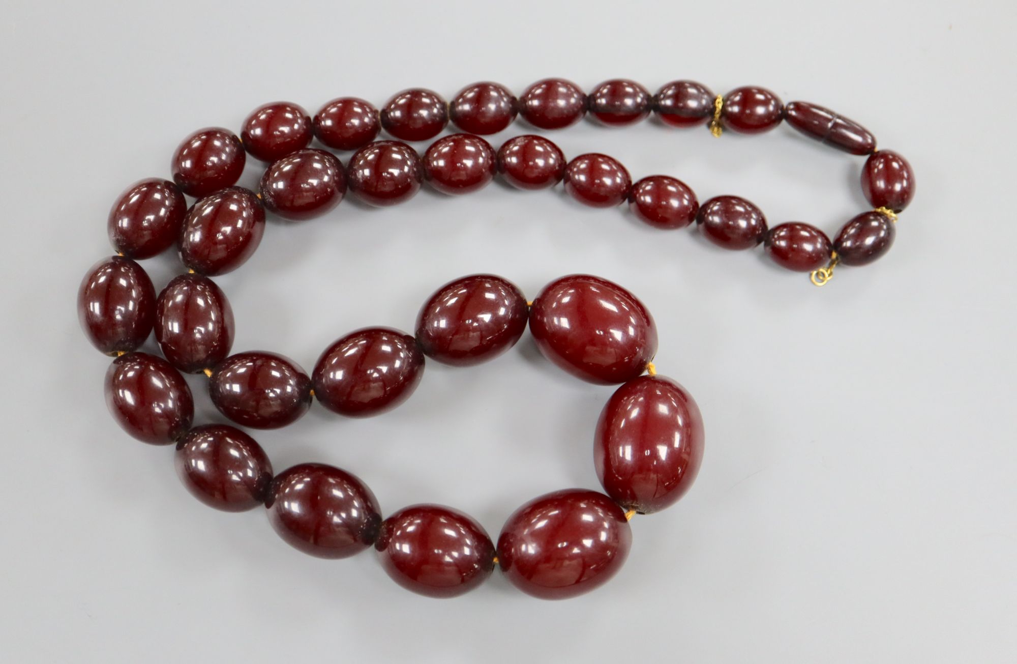 A single strand graduated simulated cherry amber oval bead necklace, 61cm, gross weight 99 grams.